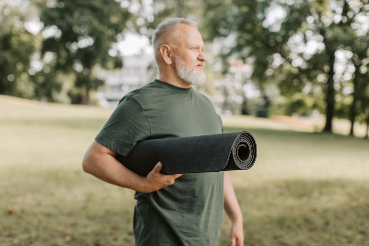 Homme d’une cinquantaine d’années avec un tapis de yoga sous le bras dans un parc