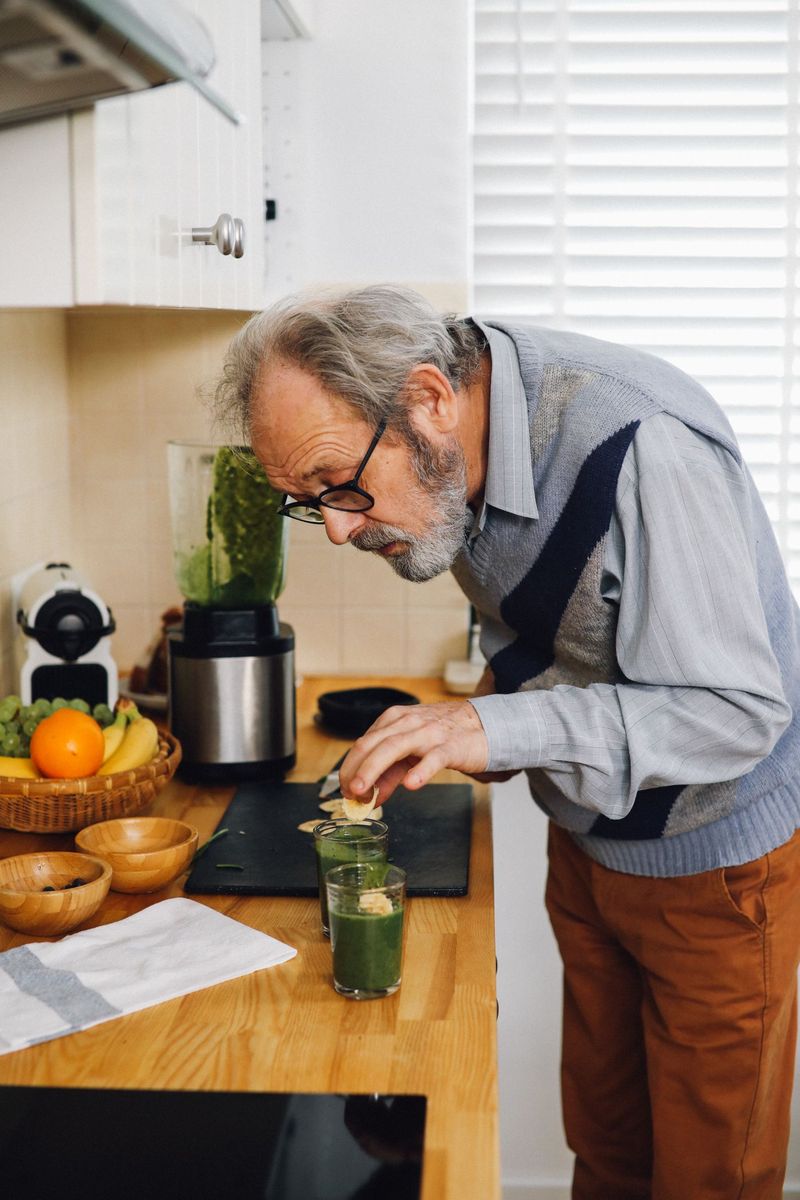 Homme âgé qui prépare un smoothie vert dans sa cuisine