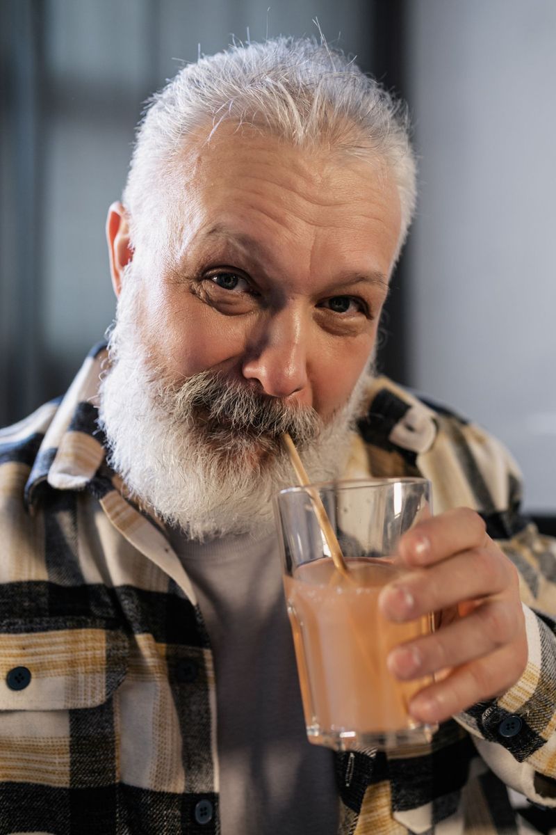 Homme âgé à la barbe grise qui boit un smoothie avec une paille