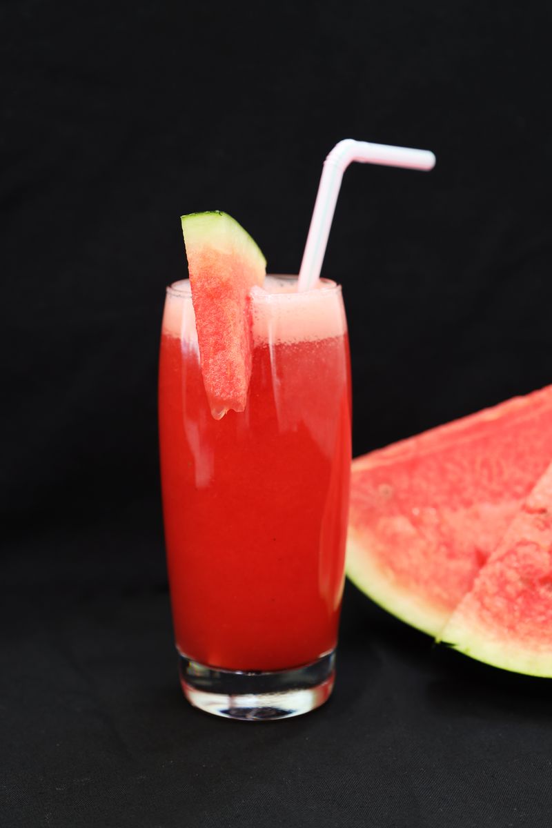 Verre de jus de pastèque avec une paille à côté d’une tranche de pastèque